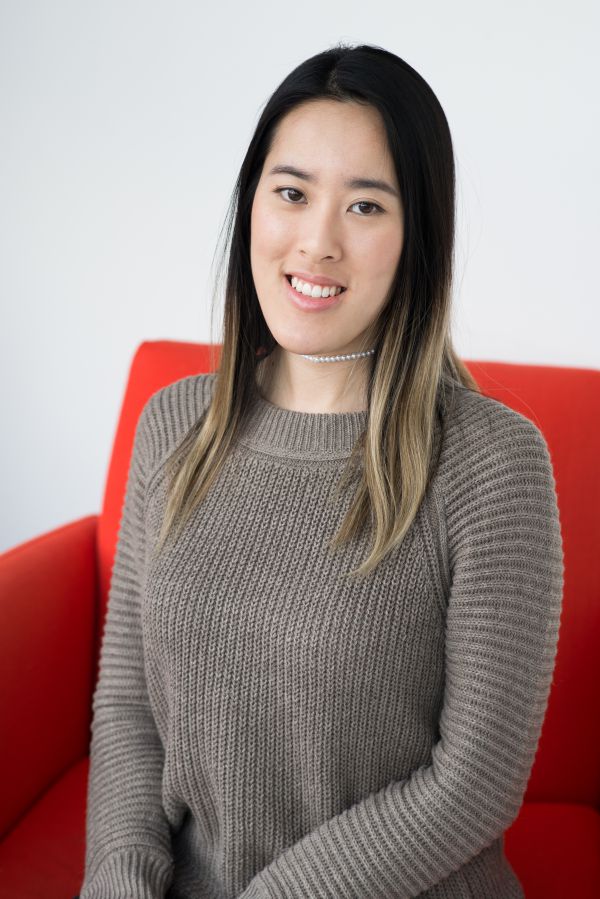 A headshot of Jessica Ho, sitting in a red chair, smiling