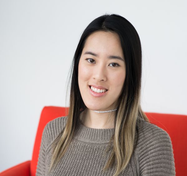 A headshot of Jessica Ho, sitting in a red chair, smiling